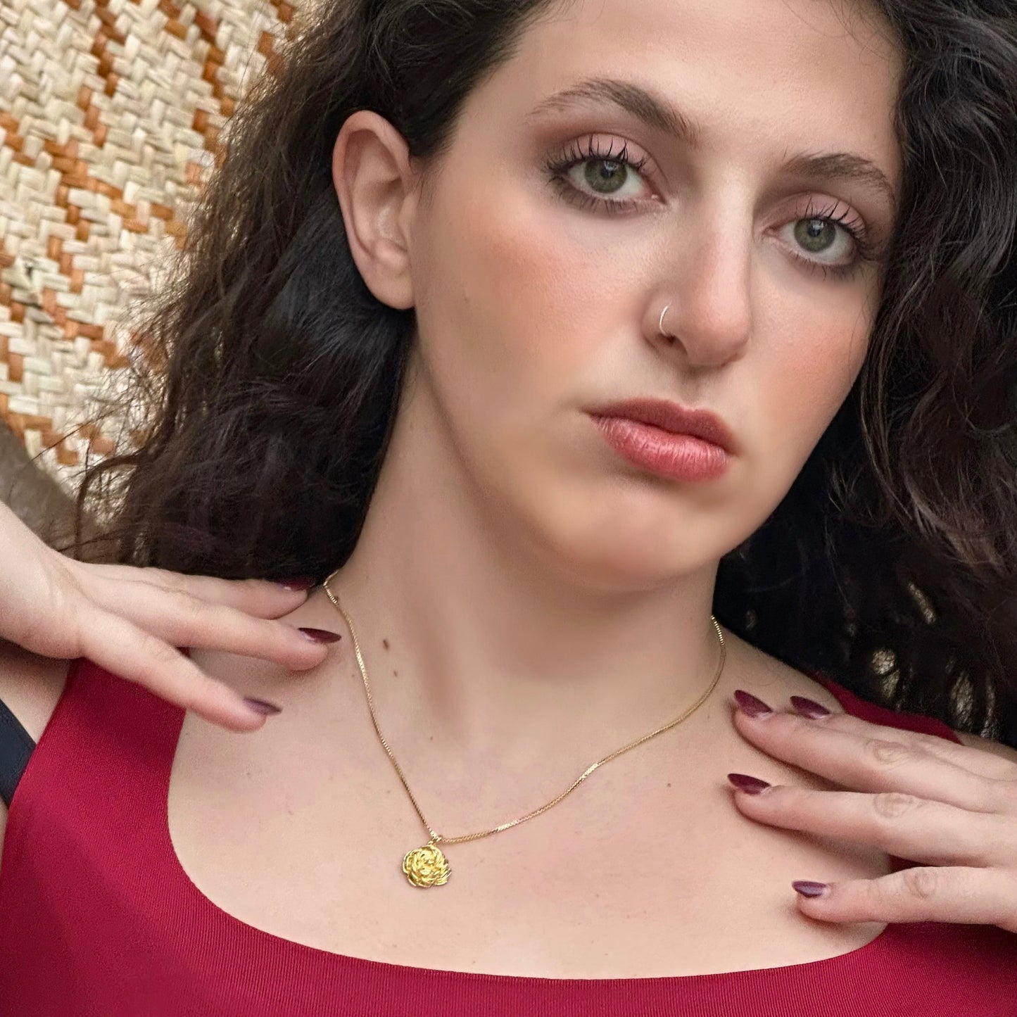 Woman wearing a gold necklace with a heart pendant, set against a textured wall.
