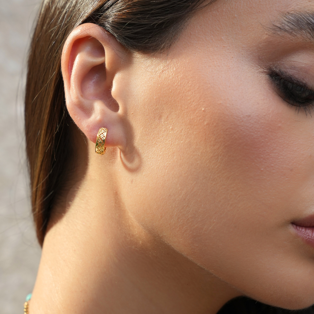 Close-up of a person wearing gold hoop earrings with a neutral background