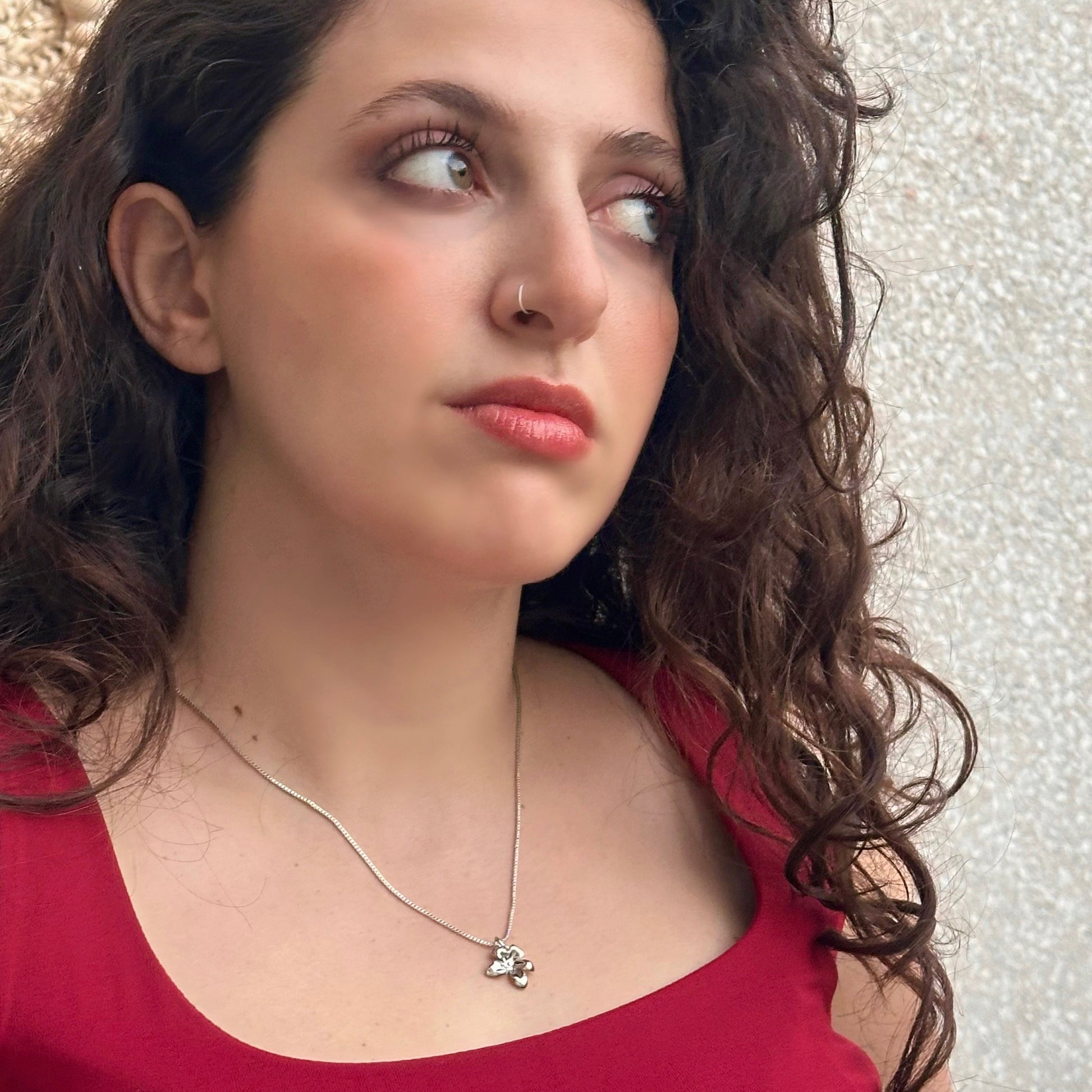Woman wearing a red top and necklace with a textured wall background
