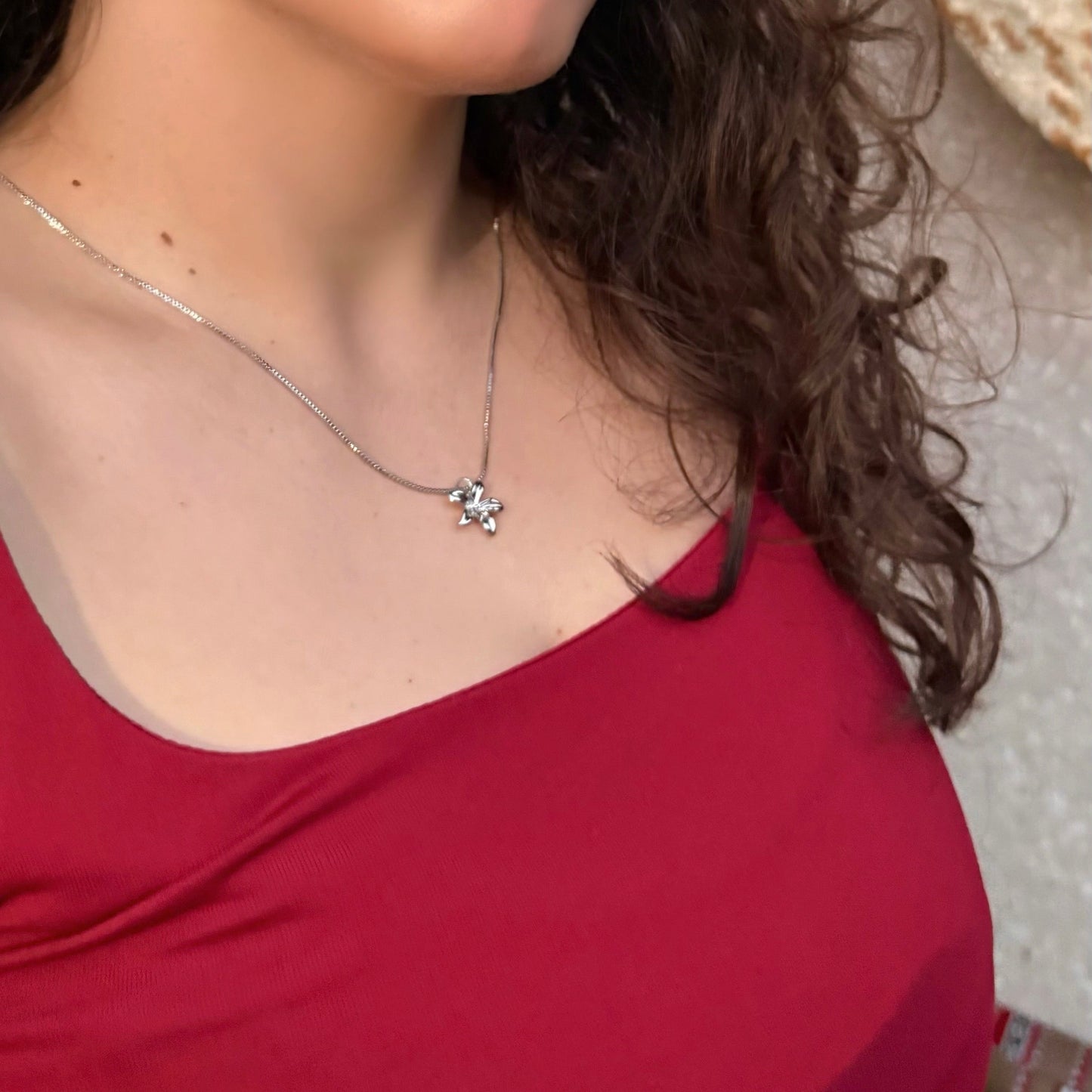 Woman wearing a red top with a necklace, looking to the side.
