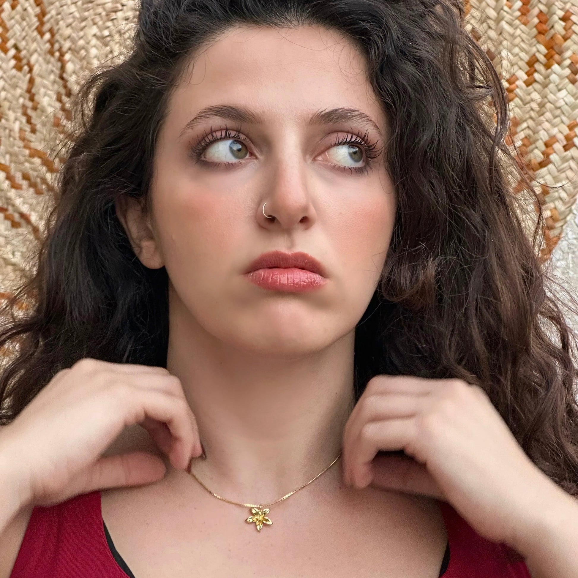 Woman wearing a gold necklace with a red top against a textured wall.