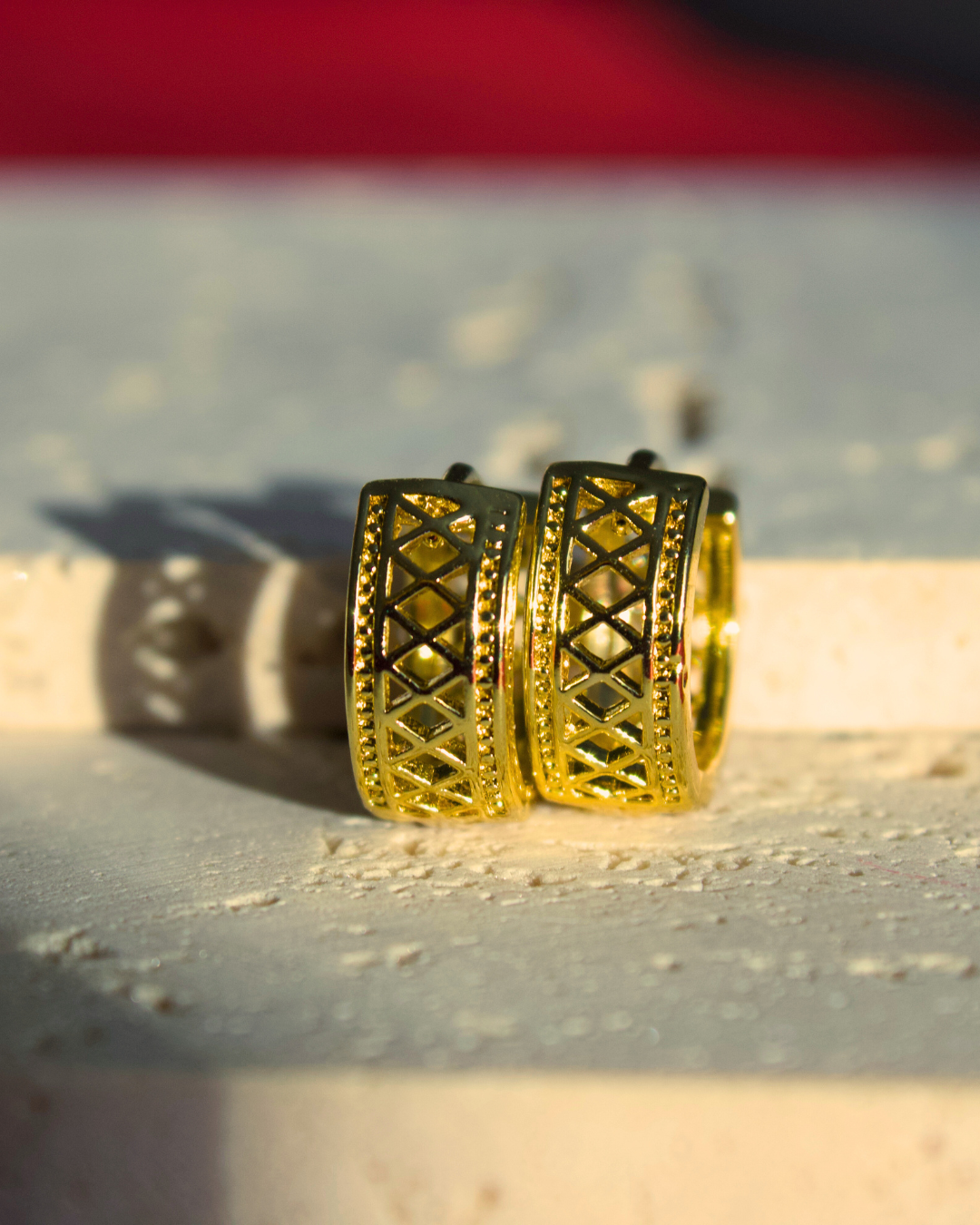 Gold hoop earrings named Marrakesh from ARDI on a textured surface with a blurred background